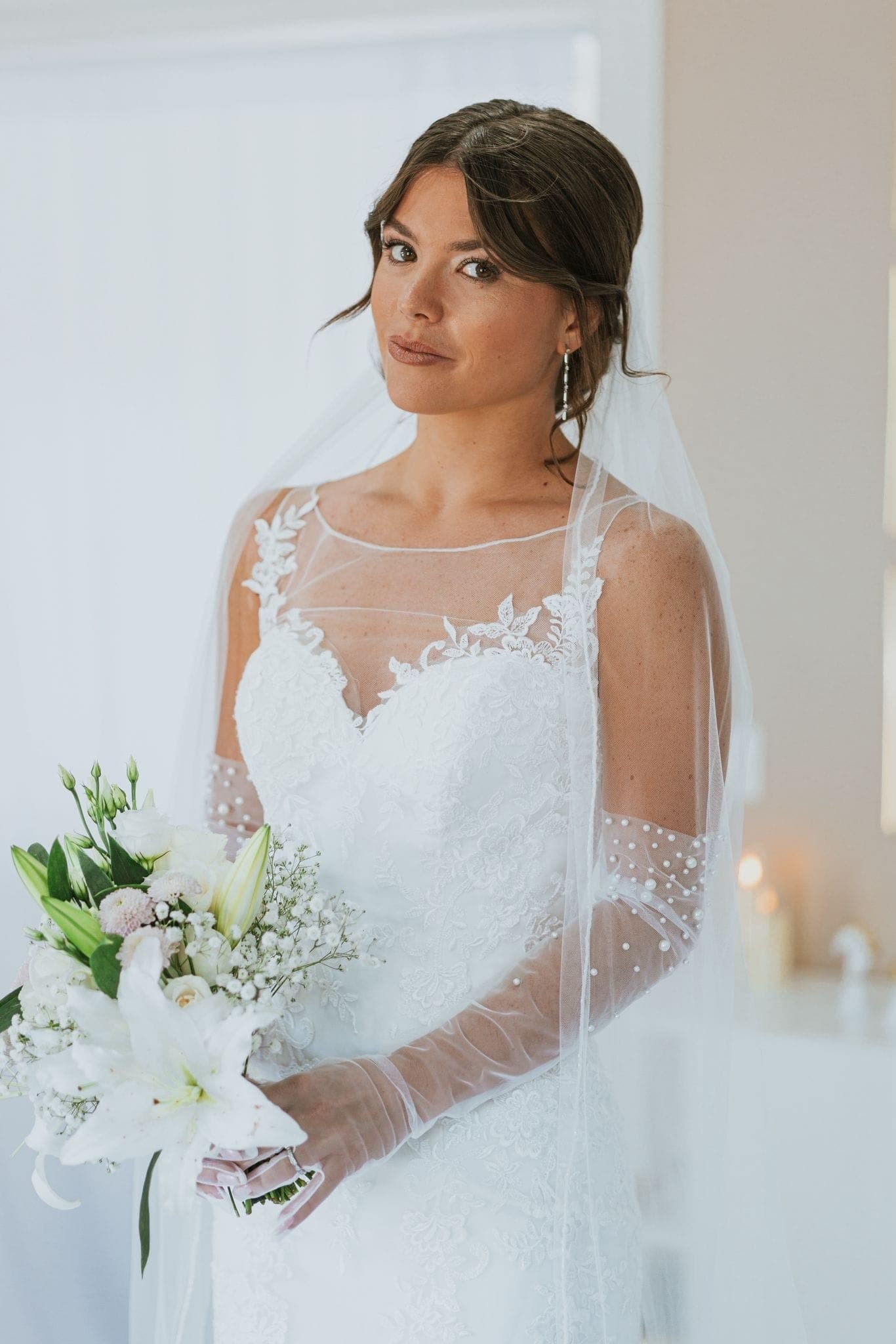 Gros plan sur une coiffure de mariée ornée de perles, bouquet à la main